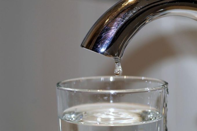 Glass of water beneath a faucet.